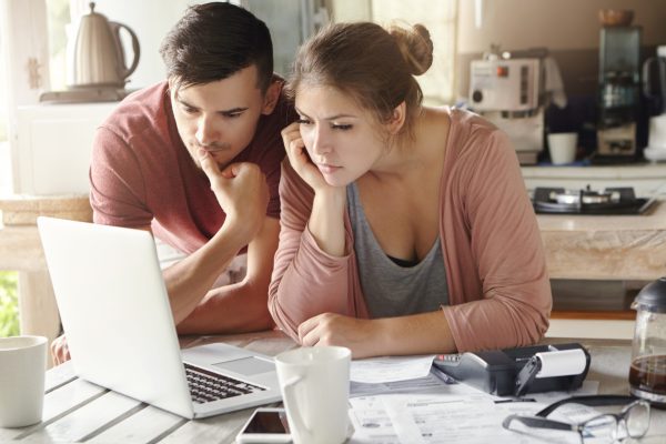 Serious,Man,And,Woman,Sitting,At,Kitchen,Table,In,Front